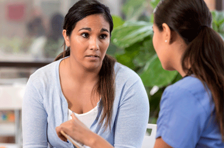 A healthcare worker is speaking to a woman who looks concerned.
