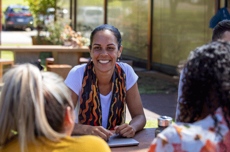 A woman is sitting at a table with other people. She is smiling.